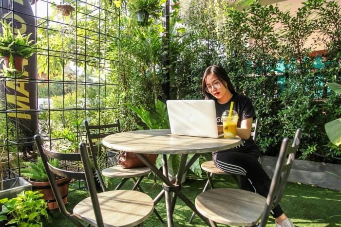 A woman sat at a table in a botancial garden with her laptop